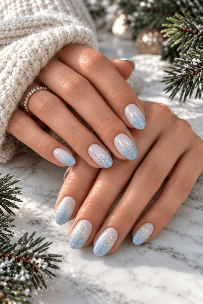 woman's hands showing a soft white-to-icy-blue ombré manicure with subtle shimmer, white marble surface, a few evergreen branches nearby, realistic natural-light photography